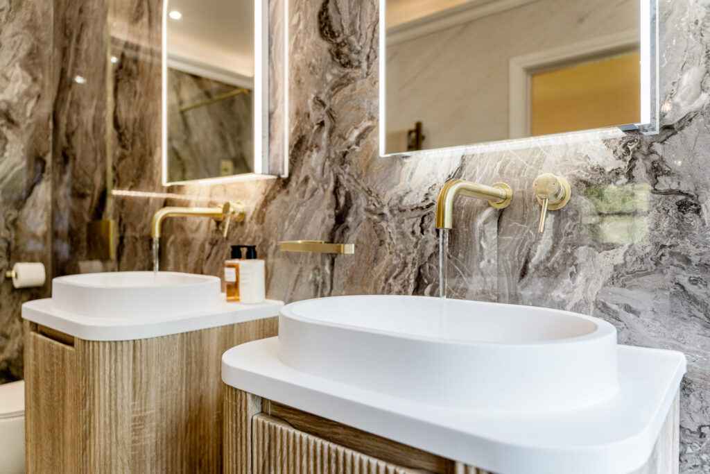 Marble bathroom with twin basins and brass taps at 5 Holland Park, Bramhall